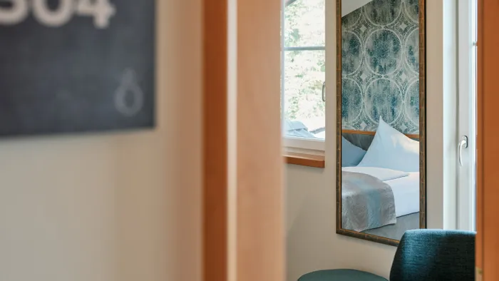 Hotelzimmer 304 mit Bett und gemusterter Wand im Spiegel neben dem Fenster gespiegelt